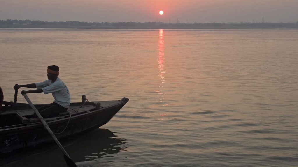 A boatman rowing a wooden boat on the Ganga at sunrise near Assi Ghat