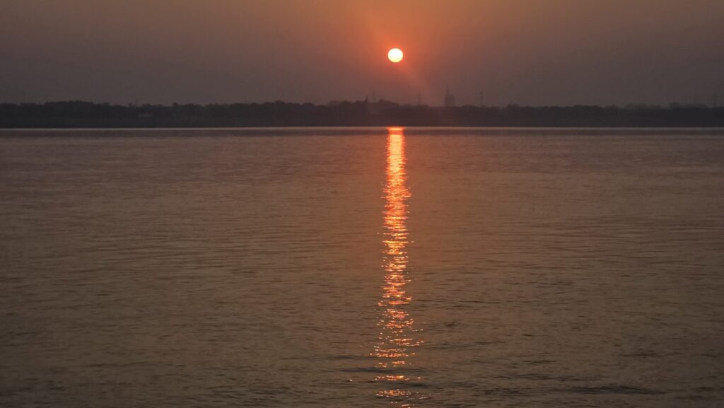The sun rising over the Ganga with its reflection on the water, seen from Assi Ghat
