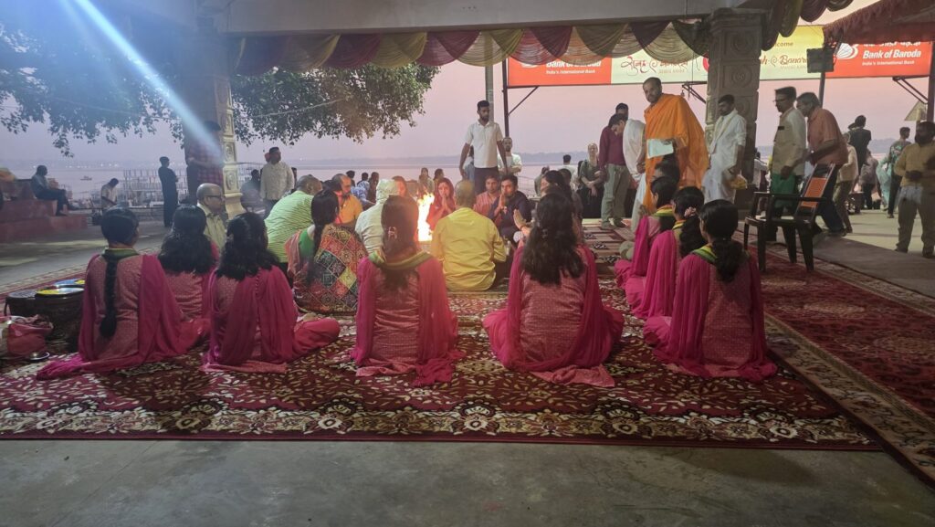 Participants seated around the havan fire under a canopy at Assi Ghat in the early morning